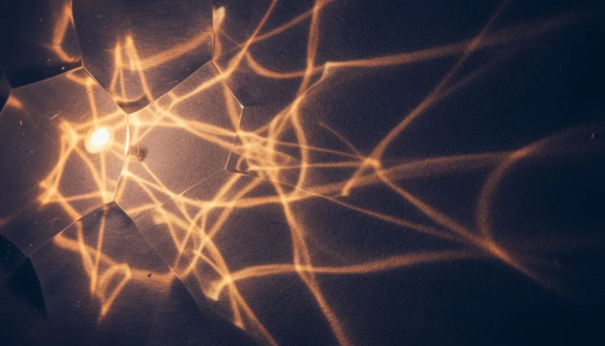 Réseau de filaments lumineux orangés rayonnant depuis un point de lumière unique, sur fond sombre